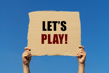 Let's play text on box paper held by 2 hands with isolated blue sky background. This message board can be used as business concept to let start playing.