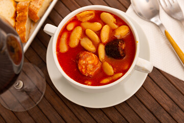 Hearty beans stew with pork, blood sausage and chorizo served in white bowl. Traditional dish of...