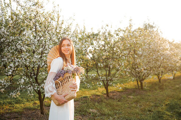 Amazing young woman in a straw hat posing in a garden of flowering trees in spring.