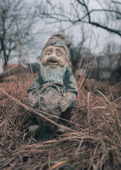 Old garden gnome figure with peeling paint among dry grass. Garden decor. Retro style. Home street decor. The figure of a gnome. Peeled paint.