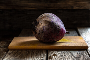 A whole beetroot with a peel on a cutting board on a dark background. Home cooking in the kitchen.