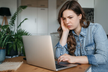 Sad woman looking annoyed and stressed, sitting at the desk, using a laptop, thinking, feeling tired and bored with depression problems