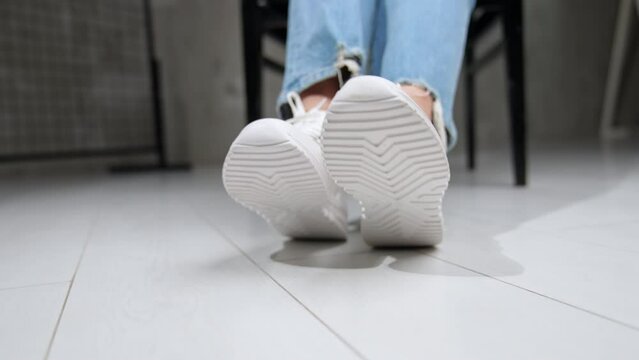 Model wears white comfortable sport shoes. Girl stretches feet closer to camera demonstrating footwear soles. Close up.