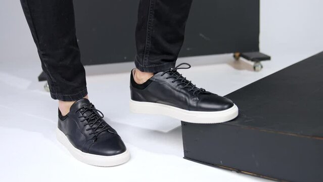 Male feet in black jeans and black shoes on white soles. Model steps on a step to demonstrate footwear. Close up.