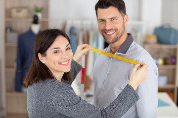 female tailor taking measurements of male customer