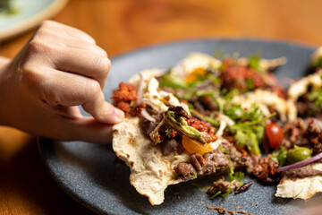 Mexican dish tlayuda, held with one hand, about to be eaten.