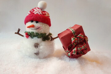 Snowman with Red Cap and Red Kraft Gift Box with Plaid Bow, Snow in Christmas Tradition