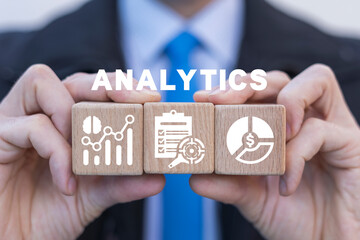 Businessman holding wooden cubes with icons and sees text: ANALYTICS. Analytics big data industry...