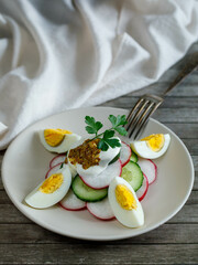Plate with healthy spring vegetarian salad with radish, cucumber, egg and parsley with sour cream. and mustard, top view on wooden background with fork and napkin, russian summer food. Vertical