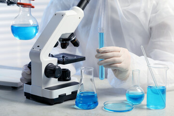 Scientist with test tube of light blue liquid near microscope in laboratory, closeup