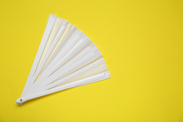 White hand fan on yellow background, top view. Space for text