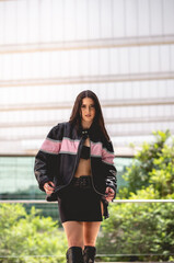Urban chic: young brunette model wears leather jacket and long boots in public park with morning...