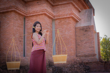 Beautiful thai woman in traditional thai dress is holding a hawker basket and looking to the camera in an old temple with a smile.