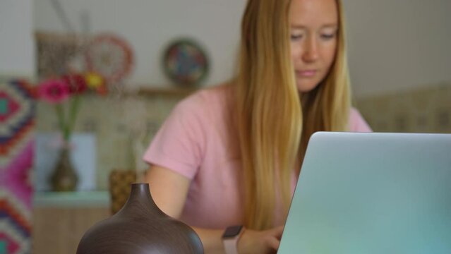 The video features a young woman sitting at a desk in her apartment, working on her laptop. A working electric aromatherapy diffuser is seen to the side of her, emitting a soothing fragrance. The