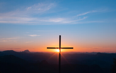 Silhouette of a Christian cross with sunset light in the background symbolizing faith, forgiveness,...
