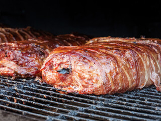 Delicious smoked minced meat patty rolls wrapped in bacon on the smoker grate