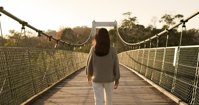 Woman walk over the suspension wooden bridge in countryside