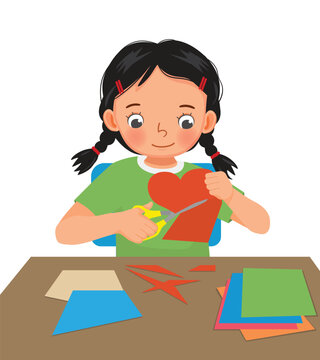 Cute little girl cutting colored paper with scissors making heart shape paper cut art craft