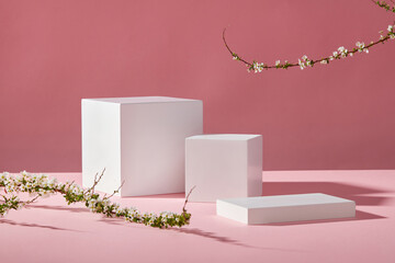 Three white empty podiums and white flower branches on pink background. Minimal art background with copy space for cosmetics and product presentation. Front view.