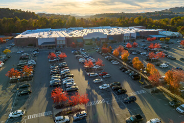 Top view of many cars parked on a parking lot in front of a strip mall plaza. Concept of consumerism and market economy