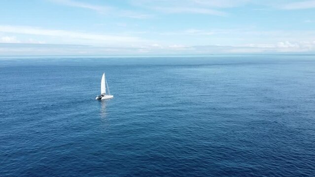 Flying towards a small yacht as it slowly sails through a flat ocean
