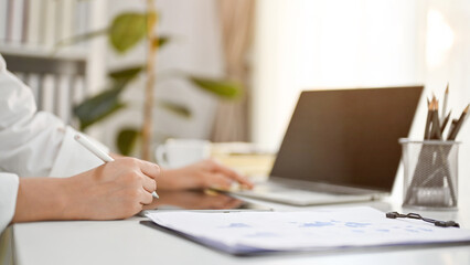 Cropped side view image of a businesswoman working at her desk, using laptop and tablet