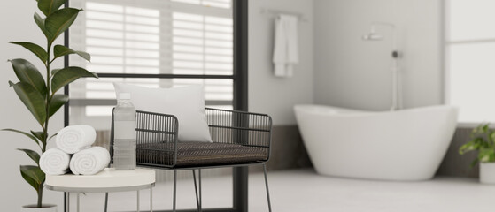 Modern stylish armchair, side table with towels and a bottle of water in modern white bathroom