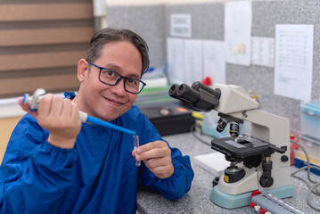 An experienced asian male laboratory technician or microbiologist using a pipette to transfer a small sample into a test tube.