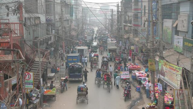 Numerous cars, motorcycles, rickshaws, and pedestrians driving and walking through a busy road in Dhaka, Bangladesh.