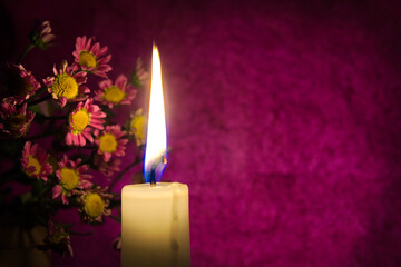 Close up of yellow wax candle flame and flowers