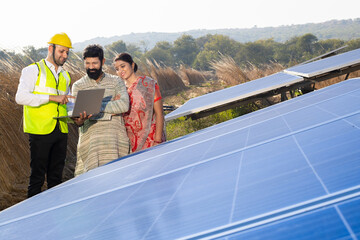 Indian engineer with laptop talking to young couple about solar panel installation. renewable green...