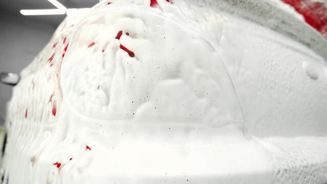 Close-up of the rear light of a car covered in foam. Active foam for contactless car wash. Car wash or car detailing process
