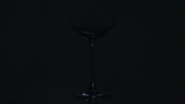 A clear wine glass momentarily being flashed by stripy light paterns. The patterns are moving quickly across the dark background High quality 4k footage