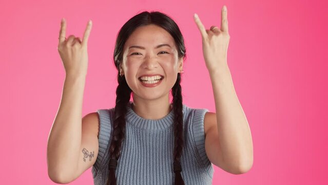 Rock, music and metal with asian woman in studio and for trendy, punk and crazy isolated on pink background. Edgy, track and happiness with girl and hand sign for positive, funky and carefree