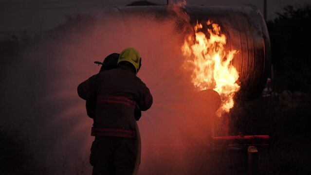 Rear view of Asian fireman wear fire protection suit. Firefighter spray water fighting at Fire station at night. Fire Fighting and Fire Drill Training Concept.