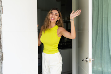Fototapeta na wymiar Welcome. Portrait of cheerful woman standing in doorway of modern apartment, greeting visitor and inviting guest to enter her home, happy