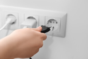 Woman putting plug into socket at home, closeup
