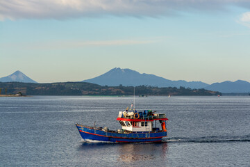 Barco de pesca al atardecer. Al fondo Volcanes Osorno y Calbuco, Chile