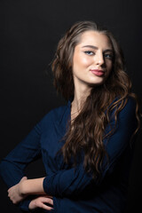 Fototapeta na wymiar Makeup and fashion concept. Brunette woman with long wavy hair sensual studio portrait. Model wearing blue blouse and looking at camera with blue eyes and seductive look. Dark studio background