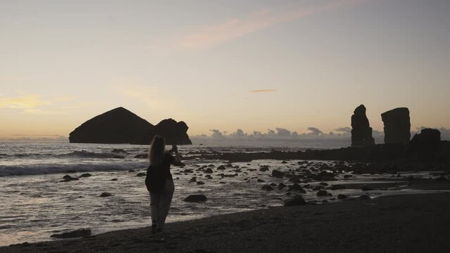 Woman takes pictures of rocky horizon from Azores beach, wide handheld