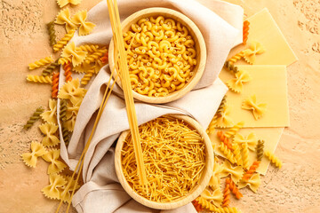 Composition with bowls of different types of raw pasta on color background