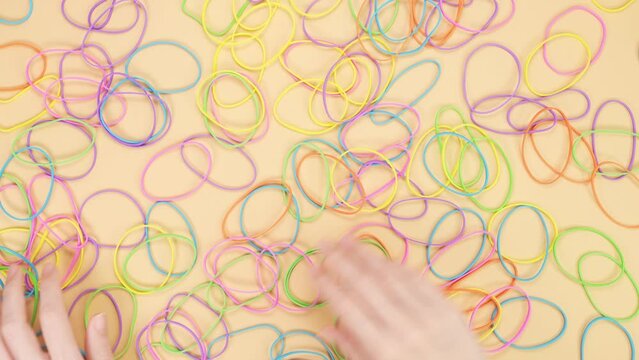 Hands choosing only 5 colors of elastic rubber bands from bunch of colorful rubber bands on yellow background. Bright office rubber bands. Multicolored elastic rubber bands close up.