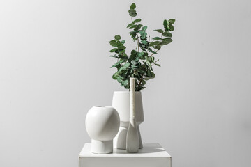 Vases with eucalyptus branches and candle on table near grey wall