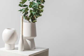 Vases with eucalyptus branches and candle on table near grey wall