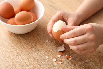Woman peeling boiled egg on wooden table, closeup