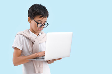 Little boy in eyeglasses using laptop on blue background