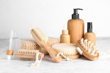 Different massage brushes, sponge and bottles of cosmetic products on light background