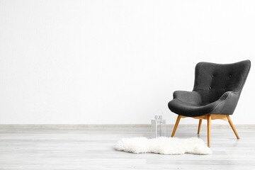Stylish grey armchair, fur rug and lantern near white wall