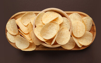 Board and bowl with delicious potato chips on brown background