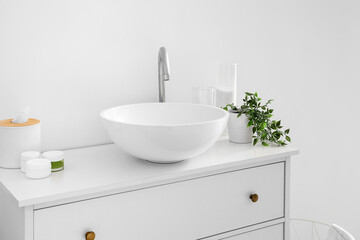 Obraz na płótnie Canvas Sink with bath accessories, candles and houseplant on chest of drawers near light wall